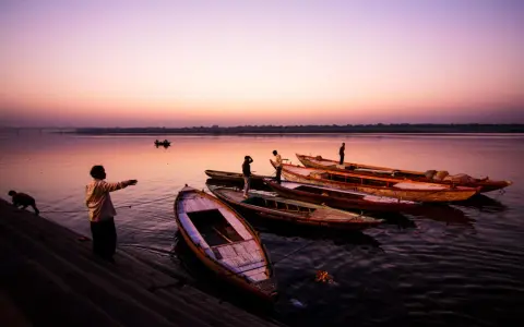 Vue d'ensemble de bateaux amarrés sur un fleuve au crépuscule, avec des silhouettes humaines sur la rive. Ces photos grand angle capturent la sérénité du moment.