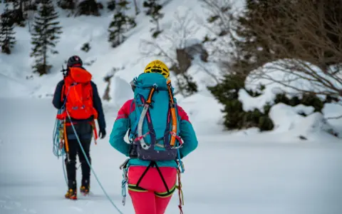 Dwóch alpinistów w zimowych strojach, z plecakami i sprzętem, przemierza ośnieżony teren. To inspiracja, co zabrać w góry zimą.