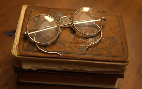 Stare okulary na zabytkowej księdze, jakbyśmy cofali się do czasów, kiedy wynaleziono okulary przeciwsłoneczne.