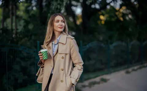 Donna con trench beige, un classico del marchio Burberry, sorseggia un caffè all'aperto.
