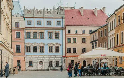Kolorowe kamienice na rynku, idealne na tani city break. Ludzie spacerują, siedzą w ogródku kawiarnianym.
