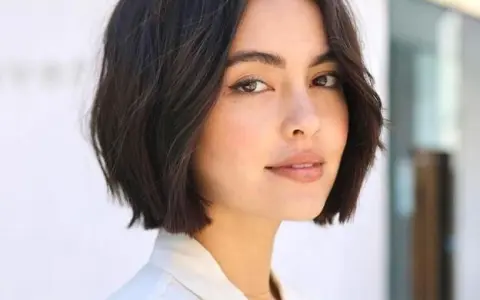 Mujer con un moderno corte de pelo bob oscuro y ondulado, luciendo un estilo chic y juvenil.