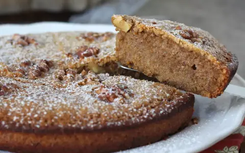 Une part est soulevée d'un délicieux gâteau aux noix, saupoudré de sucre glace.