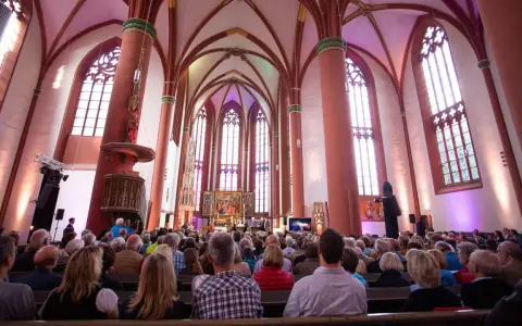Menschen sitzen in einer Kirche, die für eine Veranstaltung beleuchtet ist. Es ist schön, dass man wieder in die Kirche eintreten kann.