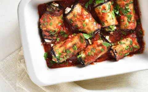 Involtini di melanzane ripieni di formaggio, cotti in sugo di pomodoro e guarniti con prezzemolo fresco.