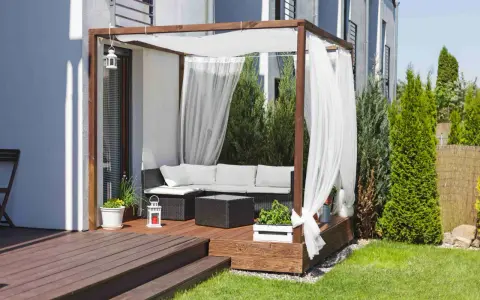 Drewniana pergola z białymi zasłonami to idealne miejsce na tarasie. Zasłony powieszone na drewnianej konstrukcji tworzą przytulną atmosferę.