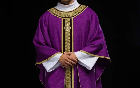 Eleganckie fioletowe szaty liturgiczne z bogatymi złotymi zdobieniami, noszone przez mężczyznę z dłońmi złożonymi na piersi.