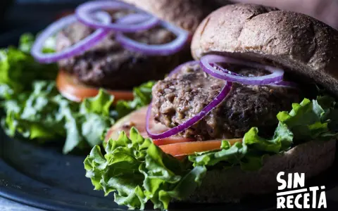 Dos deliciosas hamburguesas de lentejas con lechuga fresca, tomate y aros de cebolla morada, listas para disfrutar.