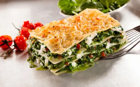 Deliciosa lasaña de verduras, con capas de pasta, espinacas y queso cremoso, acompañada de tomates cherry.