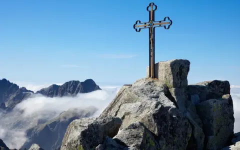 Krzyż na skalistym szczycie Gerlach. Widok na Tatry Wysokie ponad morzem chmur.