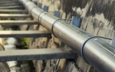 Długi, metalowy rurociąg biegnie wzdłuż betonowego koryta. To ważna kanalizacja tłoczna, transportująca płyny.