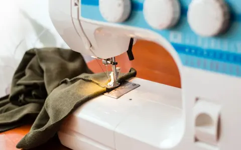 Maszyna do szycia z zieloną tkaniną. Zastanawiasz się, dlaczego maszyna do szycia zrywa górną nitkę? Może problem tkwi w igle lub naprężeniu?