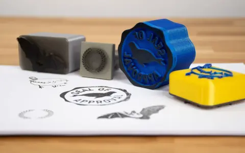 A blue 3d print stamp with a seal of approval design sits next to a yellow one.