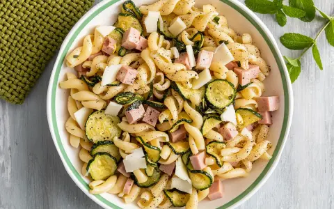 Un'insalata di pasta fredda sfiziosa con fusilli, zucchine grigliate, cubetti di prosciutto cotto e scaglie di formaggio.