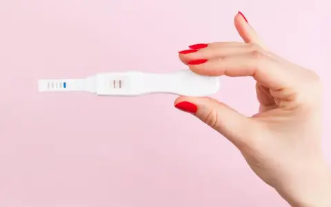 Dłoń z czerwonymi paznokciami trzyma test ciążowy z dwoma kreskami. To może być sygnał, że doszło do ciąży biochemicznej.