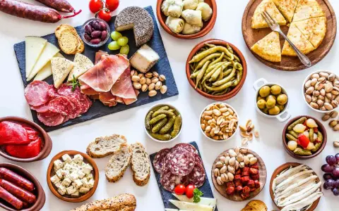 Una mesa llena de aperitivos baratos para mucha gente: embutidos, quesos, aceitunas, frutos secos, pimientos, pepinillos y pan.