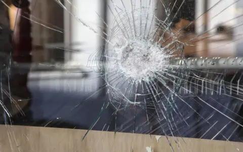 Une étoile de verre brisé se propage à travers la vitre, révélant un monde flou derrière.