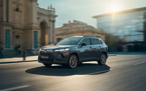Ciemnoszary Toyota Corolla Cross sunie ulicą miasta, mijając zabytkowe budynki i nowoczesne szklane fasady.