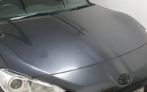 A dark grey car hood with a Toyota emblem. The paint has some minor imperfections, hinting at the question: how long does it take to clay bar a car?