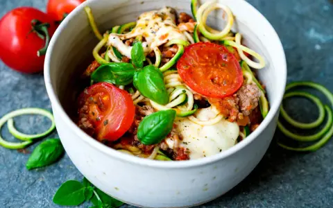 Herzhafte rezepte mit zucchini und hackfleisch: Zoodles mit Hackfleischsauce, Tomaten und geschmolzenem Käse, garniert mit frischem Basilikum.
