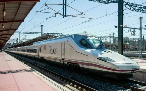 Moderner, weißer Renfe ave zug mit lila Akzenten steht auf Gleisen unter einem Bahnhofsdach.