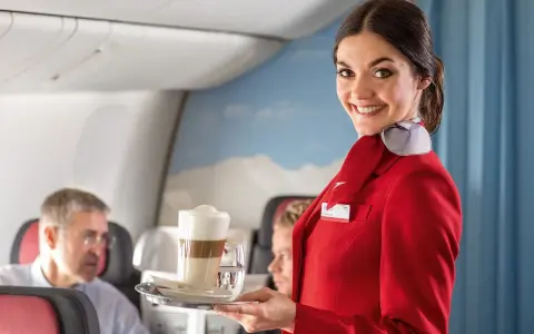 Uśmiechnięta stewardessa w czerwonym mundurku podaje kawę. Czy jej stewardessa zarobki są wysokie?
