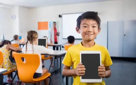 Un bambino sorridente in classe mostra un tablet, pronto per le attività di accoglienza di un nuovo alunno.
