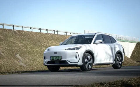 Biały SUV Geely E5 (EX5) na tle wiaduktu i niebieskiego nieba.