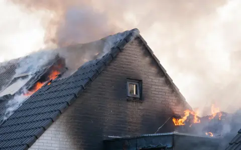 Un incendie maison ravage le toit, des flammes vives et une épaisse fumée s'échappent des tuiles.