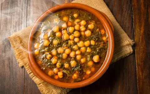 Cazuela de barro con garbanzos y espinacas, humeante y lista para servir. Se puede poner cazuela de barro en la vitro para cocinar este delicioso plato.