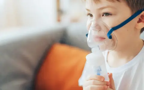 Chłopiec z maską inhalacyjną na twarzy, korzystający z nebulizatora. Pomaga mu to w leczeniu kataru.
