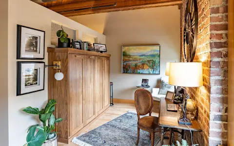 Accogliente angolo studio con un armadio a scomparsa in legno, un tappeto persiano e un quadro paesaggistico, che evoca l'atmosfera di una piccola casa di campagna.