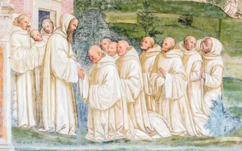 A bearded monk greets a line of novices, their white robes hinting at a rich monk history.