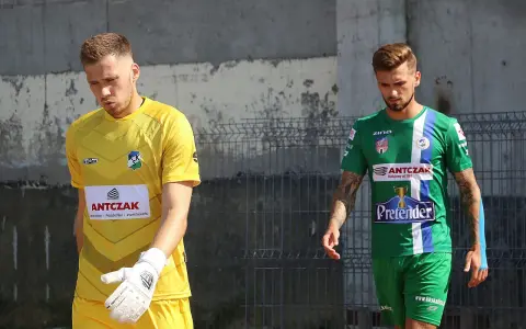 Dwóch piłkarzy, w tym Michał Kaszuba w żółtej koszulce bramkarza, idzie obok siebie.