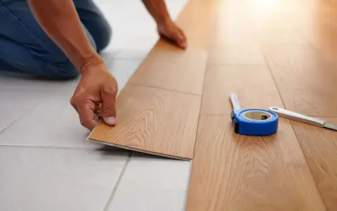Pose d'un nouveau revêtement de sol imitation bois, une solution pour niveler un sol sans ragréage. Un mètre ruban et un cutter sont à proximité.