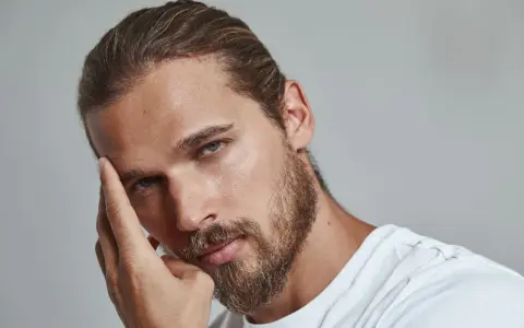 Un homme pensif, sa main effleurant son front, un sourcil plus haut que l'autre, regard intense.