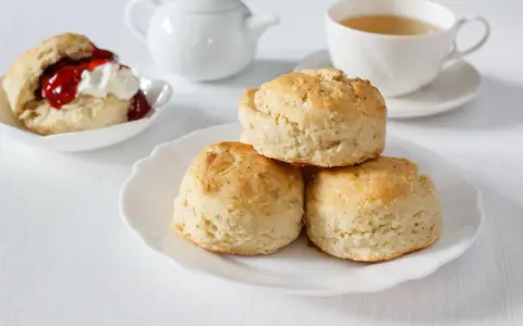 Goldbraune Scones, ein Klassiker zum Tee. Sie sind kleine, süße Gebäckstücke, die oft mit Marmelade und Sahne serviert werden.
