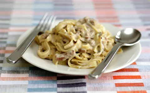 Un piatto di tagliatelle ai funghi cremose, pronte per essere gustate con forchetta e cucchiaio.