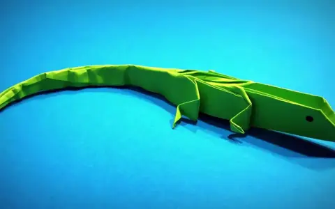 Un lagarto verde de papiroflexia animales descansa sobre un fondo azul.
