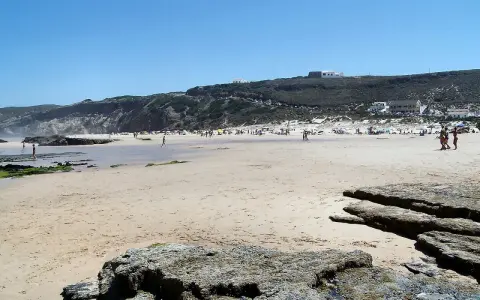 Sonniger Strand bei Monte Clerigo mit Felsen und Menschen, die sich im Wasser und am Ufer aufhalten.