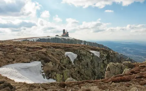 Szklarska Poręba jakie góry? Widok na Karkonosze z budynkiem na szczycie, skaliste zbocza i resztki śniegu.