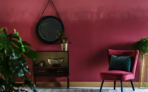 Eleganckie wnętrze w odcieniu **kolor burgundowy**. Aksamitny fotel, lustro i stylowa komoda tworzą przytulną atmosferę.