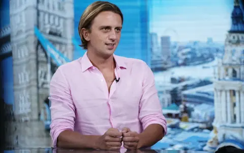 Nikołaj Storonski w różowej koszuli, na tle panoramy Londynu z Tower Bridge.