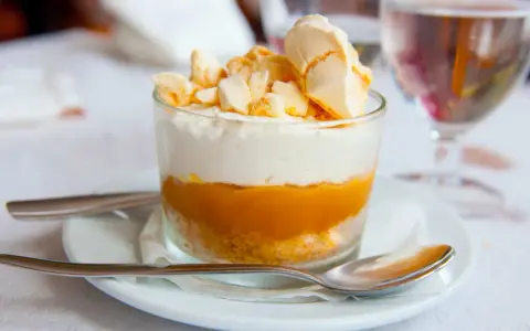 Postre en vaso con capas de galleta, crema y mermelada de mango, coronado con merengue crujiente, como un polvito canario.