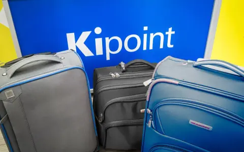 Three suitcases in front of a blue sign with "Kipoint" in white letters.