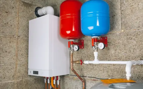 Nowoczesny kocioł z dwoma zbiornikami (czerwonym i niebieskim) i instalacją hydrauliczną. To przyszłość ogrzewania, bo zakaz pieców gazowych zbliża się wielkimi krokami.