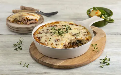 Zapiekanka makaronowa z mięsem mielonym w sosie śmietanowym, posypana serem i ziołami, podana z sałatką.