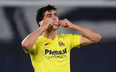 Gerard Moreno, jugador del Villarreal, celebra un gol con un gesto divertido, sacando la lengua y tocándose las mejillas.