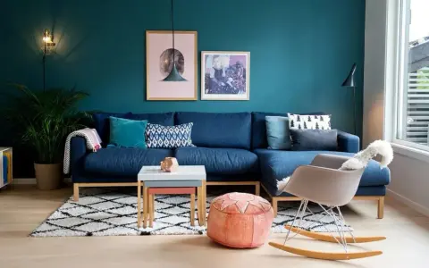 Un accogliente salotto con divano blu, tappeto a rombi e pareti color ral ottanio.