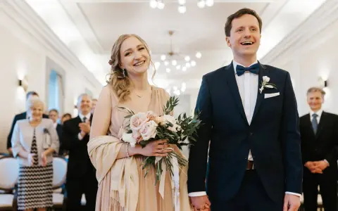 Para młoda uśmiecha się radośnie, trzymając bukiet. Złożyli wniosek o ślub cywilny i są gotowi na ceremonię.